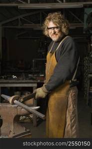 Portrait of Caucasian male metalsmith holding metal on anvil.