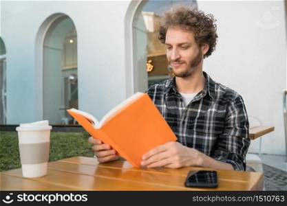 Portrait of caucasian man enjoying free time and reading a book while sitting outdoors at coffee shop.