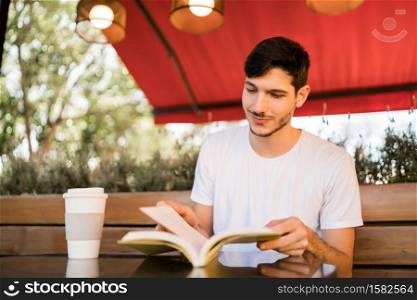 Portrait of caucasian man enjoying free time and reading a book while sitting outdoors at coffee shop. Lifestyle concept.