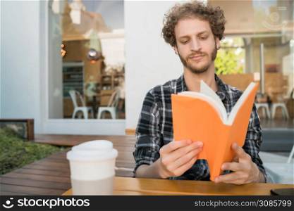 Portrait of caucasian man enjoying free time and reading a book while sitting outdoors at coffee shop.