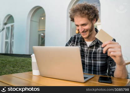 Portrait of caucasian man holding credit card and using laptop to shop online at a coffee shop. Shopping online and lifestyle concept.
