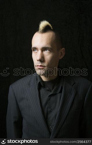 Portrait of Caucasian man in suit with mohawk against black background.