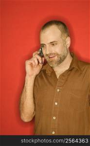 Portrait of Caucasian man talking on cellphone standing against orange background.