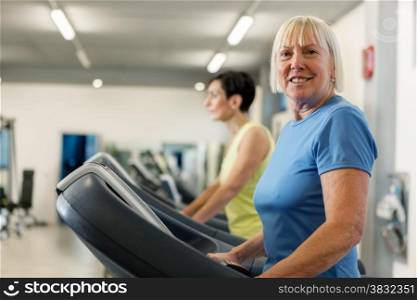 Portrait of caucasian mature woman looking towards the camera while running on a treadmill in the fitness studio