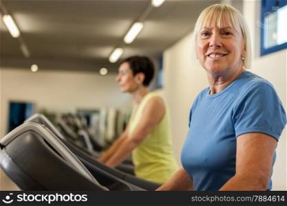 Portrait of caucasian mature woman looking towards the camera while running on a treadmill in the fitness studio