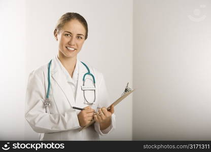 Portrait of Caucasian mid-adult female doctor writing on clipboard, smiling and looking at viewer.