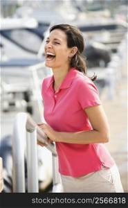 Portrait of Caucasian mid-adult female holding railing and laughing at harbor.