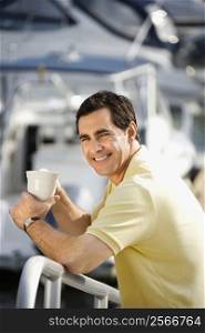 Portrait of Caucasian mid-adult male holding coffee cup at harbor looking at camera.
