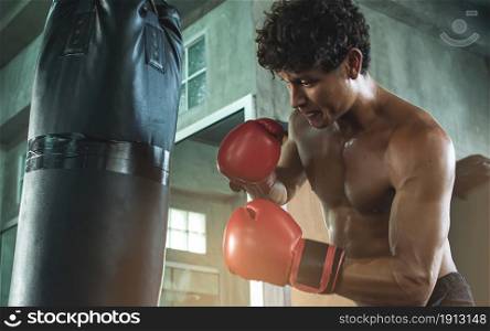 Portrait of Caucasian muscular man wearing red boxing glove and punching bag while exercising in gym. Sport concept.