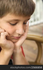 Portrait of Caucasian pre-teen boy with chin in hands looking down.