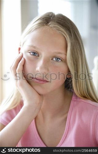 Portrait of Caucasian pre-teen girl looking at viewer resting chin in hand.