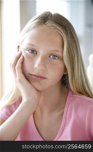 Portrait of Caucasian pre-teen girl looking at viewer resting chin in hand.