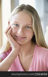 Portrait of Caucasian pre-teen girl looking at viewer resting chin in hand and smiling.
