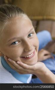 Portrait of Caucasian pre-teen girl with chin in hand looking at viewer and smiling.