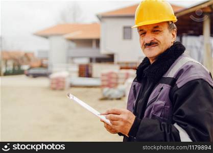 Portrait of caucasian senior man construction worker general laborer building contractor wearing yellow protective helmet holding pen and document checking data report project on the site