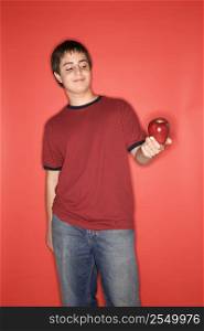 Portrait of Caucasian teen boy holding an apple standing against red background.