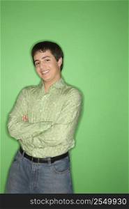 Portrait of Caucasian teen boy smiling with crossed arms standing against green background.l