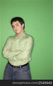 Portrait of Caucasian teen boy with crossed arms standing against green background.