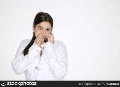 Portrait of Caucasian teen girl whispering into cellphone standing against white background.