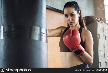 Portrait of Caucasian woman wearing red boxing glove and punching bag while exercising in gym. Sport concept.