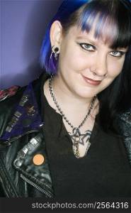 Portrait of Caucasian woman with blue hair and black leather jacket against blue background.