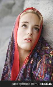 Portrait of Caucasian young adult woman with scarf draped over head looking up.
