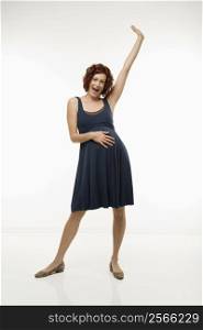 Portrait of Caucasion mid-adult attractive pregnant woman standing with one hand on belly and other arm in air looking at viewer and smiling.