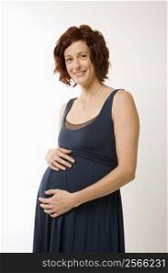 Portrait of Caucasion mid-adult pregnant woman with hands on belly looking at viewer and smiling.