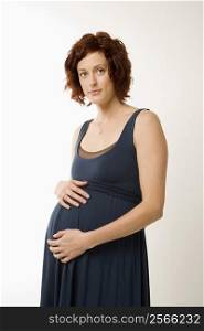 Portrait of Caucasion mid-adult pregnant woman with hands on belly looking at viewer.