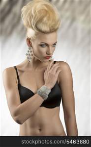 portrait of charming blonde woman with fashion hairdo and glossy jewelleries posing in lingerie. Wearing black bra