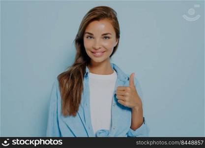 Portrait of charming confident smart female promoter recommends great decisions choice, showing thumb up sign, wears casual look outfit isolated over pastel blue colored background with copy space. Portrait of charming confident smart female promoter