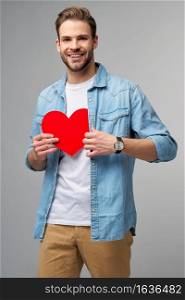 Portrait of charming man hold hand paper heart shaped card wear casual style shirt isolated over grey background.. Portrait of charming man hold hand paper heart shaped card wear casual style shirt isolated over grey background