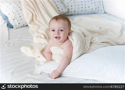 Portrait of cheerful baby boy lying on big pillow under white blanket