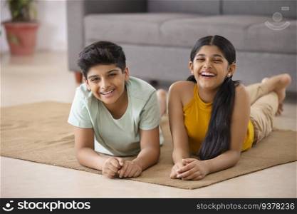Portrait of cheerful boy and girl lying down on floor in living room