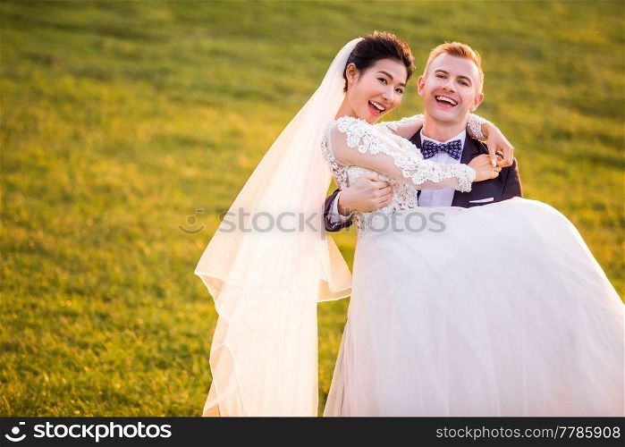 Portrait of cheerful bridegroom carrying bride on grassy field