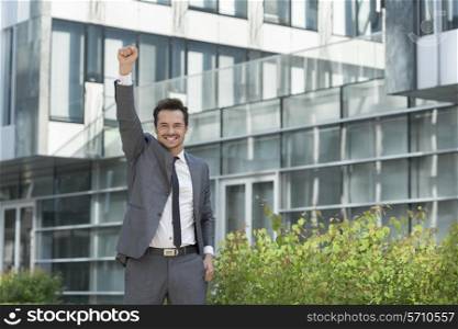 Portrait of cheerful businessman with arm raised standing outside office building