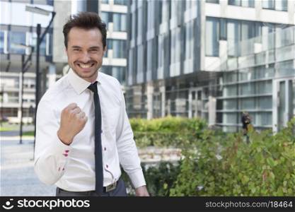 Portrait of cheerful businessman with clenched fist standing outside office building