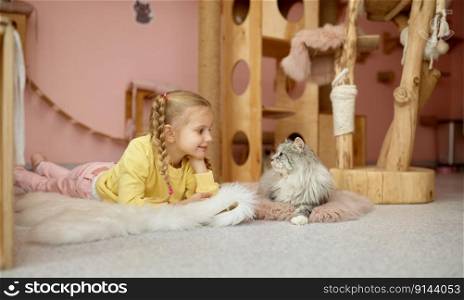 Portrait of cheerful girl lying on floor with fluffy cat over animal shelter background. Child and kitten. Cheerful girl lying on floor with fluffy cat over animal shelter background