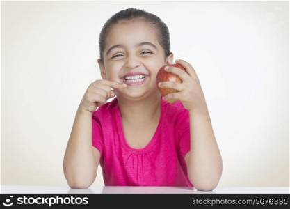 Portrait of cheerful girl showing fresh apple against colored background