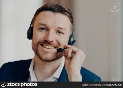 Portrait of cheerful male manager wearing headset and talking at virtual meeting during consulting client on video call, businessman smiling at camera while working in office. Job and occupation. Caucasian man in headset smiling at camera while working in office