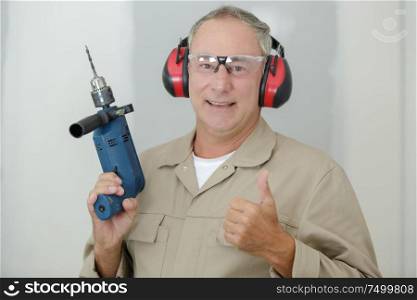 portrait of cheerful man builder with drill showing thumb-up