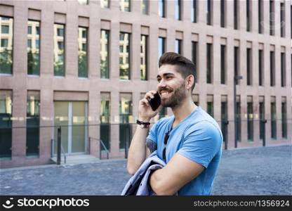 Portrait of cheerful modern businessman speaking by phone and smiling while standing outdoors