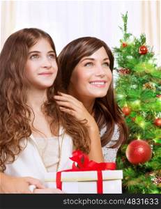 Portrait of cheerful mother and daughter with wonder looking up, celebrating holidays near beautiful decorated Christmas tree, with pleasure receiving festive gift box