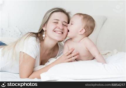 Portrait of cheerful mother hugging and kissing her baby boy on bed