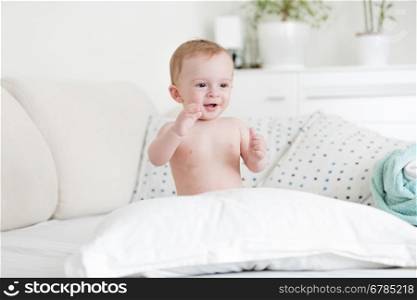 Portrait of cheerful naked baby boy playing on bed with pillows