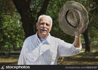 Portrait of cheerful senior man holding hat while smiling at park