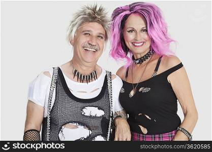 Portrait of cheerful senior punk couple with arm in arm over gray background