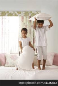 Portrait of cheerful siblings with pillows standing on bed