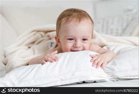 Portrait of cheerful smiling baby boy relaxing on big white pillow on bed