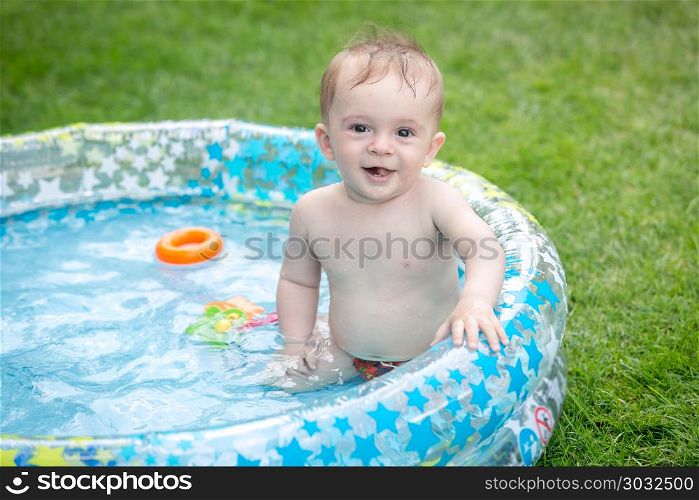 Portrait of cheerful smiling baby boy sitting in inflatable swimming pool at garden. Cheerful smiling baby boy sitting in inflatable swimming pool at garden